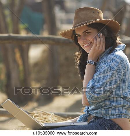Stock Image - Portrait of a teenage girl sitting with a laptop on her lap and talking on a mobile phone. Fotosearch