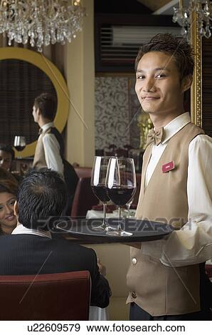 Stock Photo - Portrait of a waiter holding wine glasses in a tray. Fotosearch