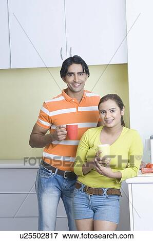 Portrait of a young couple standing in the kitchen holding coffee cups View Large Photo Image Stock Photo - Portrait of a young couple standing in the kitchen holding coffee cups. Fotosearch
