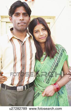 Stock Photo - Portrait of a young couple standing with their arms around each other. Fotosearch