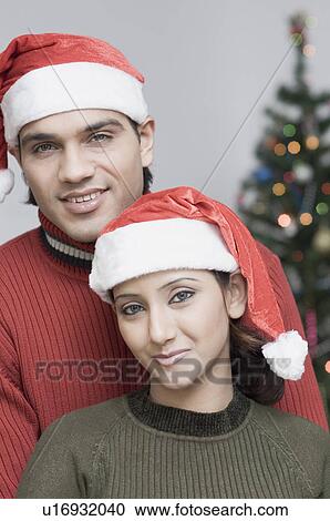 Stock Image - Portrait of a young couple wearing Santa hats. Fotosearch
