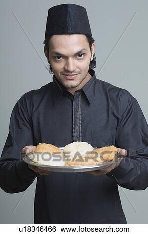 Stock Photograph - Portrait of a young man holding a plate of sweets and smiling. Fotosearch