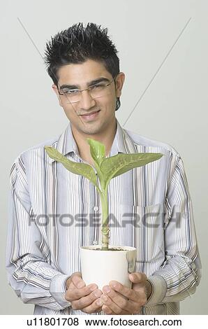 Stock Photo - Portrait of a young man holding a potted plant. Fotosearch