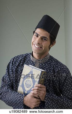 Stock Photo - Portrait of a young man holding the Koran and smiling. Fotosearch