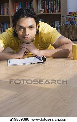 Stock Photograph - Portrait of a young man lying on the floor of a library and thinking. Fotosearch