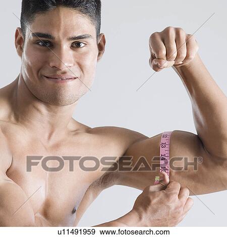 Stock Photo - Portrait of a young man measuring his biceps with a tape measure. Fotosearch