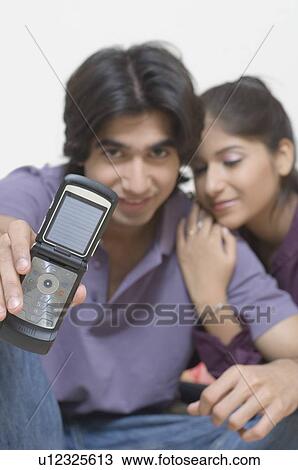 Portrait of a young man showing "I Love You" on his mobile phone with a young woman leaning on him View Large Photo Image Stock Image - Portrait of a young man showing "I Love You" on his mobile phone with a young woman leaning on him. Fotosearch