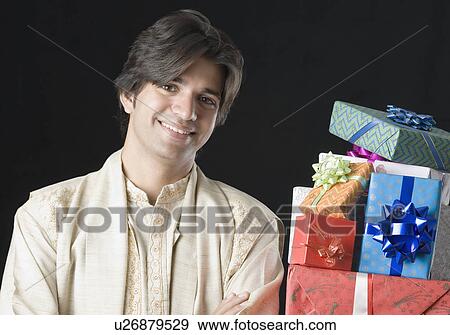 Portrait of a young man smiling with a stack of gifts beside him View Large Photo Image Stock Photo - Portrait of a young man smiling with a stack of gifts beside him. Fotosearch