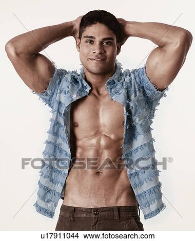 Picture - Portrait of a young man standing with hands behind his head and smiling. Fotosearch