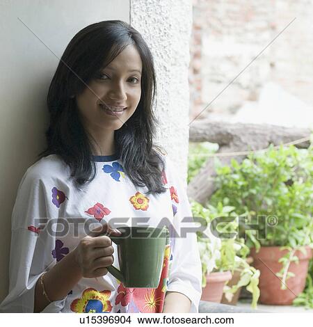 Picture - Portrait of a young woman holding a cup of coffee and smiling. Fotosearch