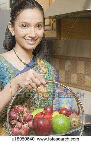 Portrait of a young woman holding a basket of fruits and smiling View Large Photo Image Stock Image - Portrait of a young woman holding a basket of fruits and smiling. Fotosearch
