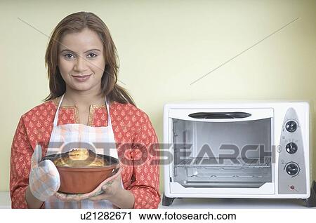 Stock Image - Portrait of a young woman holding a cake in a mould. Fotosearch