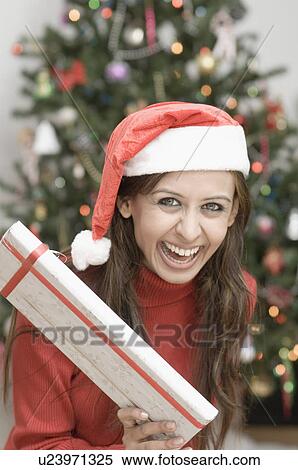 Stock Photography - Portrait of a young woman holding a Christmas present and laughing. Fotosearch