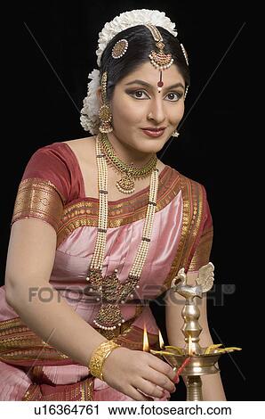Stock Image - Portrait of a young woman lighting a ceremonial lamp. Fotosearch