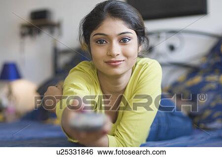 Portrait of a young woman lying on the bed and using a remote control View Large Photo Image Stock Photograph - Portrait of a young woman lying on the bed and using a remote control. Fotosearch