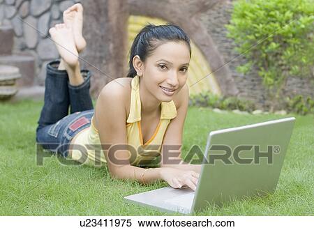 Stock Photography - Portrait of a young woman lying on the grass and using a laptop. Fotosearch