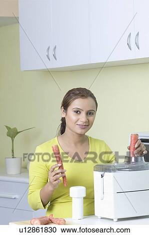 Stock Image - Portrait of a young woman making carrot juice. Fotosearch