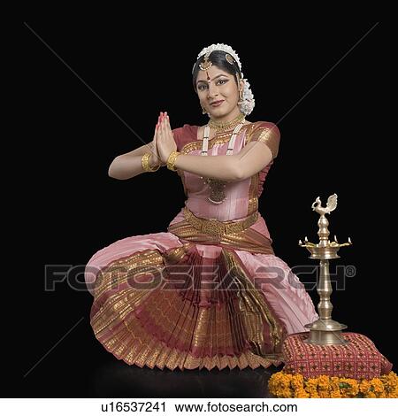 Stock Image - Portrait of a young woman performing Bharatnatyam in front of a ceremonial lamp. Fotosearch