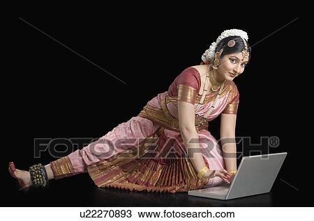 Stock Image - Portrait of a young woman performing Bharatnatyam and using a laptop. Fotosearch