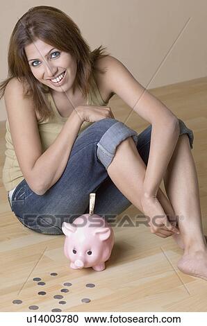 Stock Image - Portrait of a young woman sitting beside a piggy bank. Fotosearch