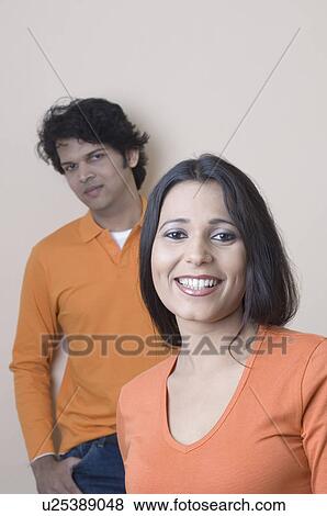 Portrait of a young woman smiling with a young man standing behind her View Large Photo Image Stock Photo - Portrait of a young woman smiling with a young man standing behind her. Fotosearch