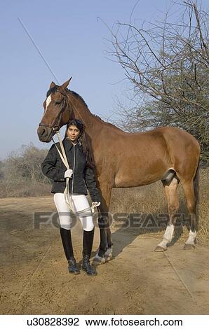 Stock Image - Portrait of a young woman standing with a horse. Fotosearch