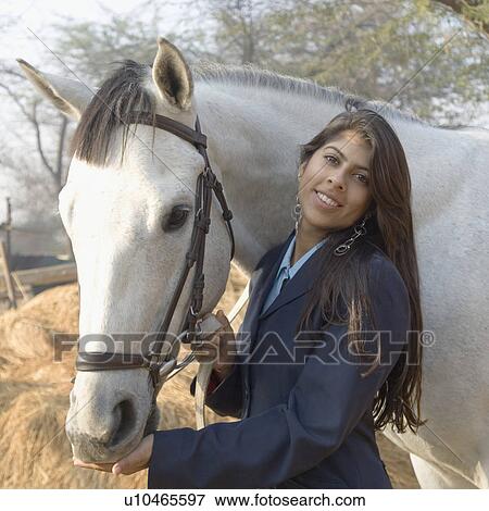 Stock Photo - Portrait of a young woman standing with a horse and smiling. Fotosearch