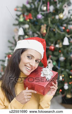 Portrait of a young woman wearing a Santa hat and holding a present View Large Photo Image Stock Image - Portrait of a young woman wearing a Santa hat and holding a present. Fotosearch