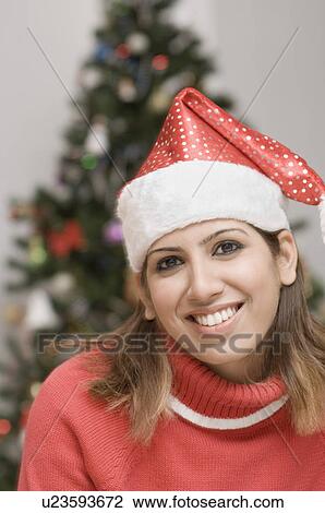 Stock Image - Portrait of a young woman wearing a Santa hat and smiling. Fotosearch