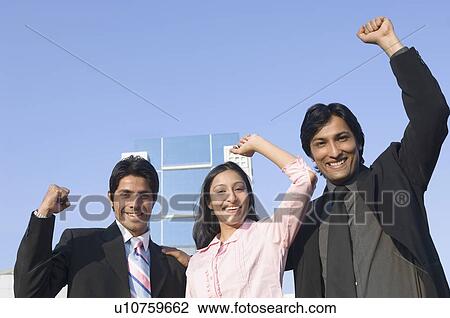 Stock Image - Portrait of two businessmen and a businesswoman smiling with their hands raised. Fotosearch