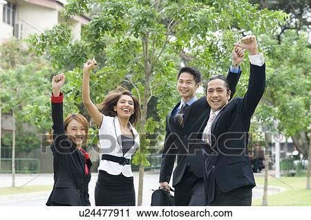 Stock Image - Portrait of two businessmen and two businesswomen raising their hands. Fotosearch