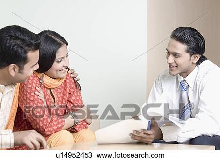 Stock Image - Real estate agent discussing a document with a young couple. Fotosearch