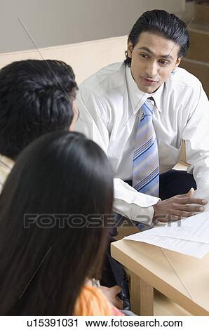 Stock Image - Real estate agent discussing a document with a young couple. Fotosearch