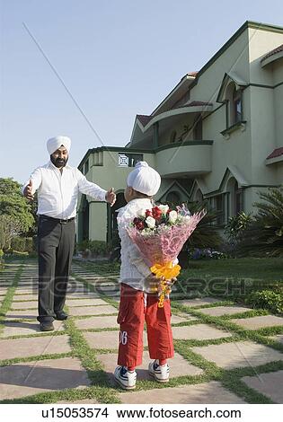 Rear view of a boy hiding a bouquet of flowers standing in front of his father View Large Photo Image Picture - Rear view of a boy hiding a bouquet of flowers standing in front of his father. Fotosearch