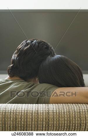 Stock Photo - Rear view of a man and a woman sitting on a couch and watching television. Fotosearch