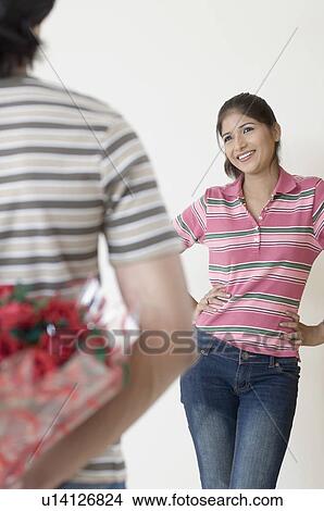 Rear view of a man hiding a bouquet of flowers from a young woman View Large Photo Image Picture - Rear view of a man hiding a bouquet of flowers from a young woman. Fotosearch