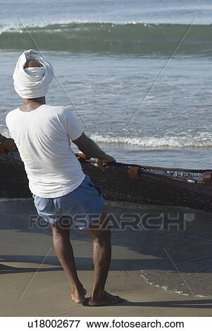Stock Photo - Rear view of a man pulling a fishing net on the beach, Morjim Beach, Goa, India. Fotosearch
