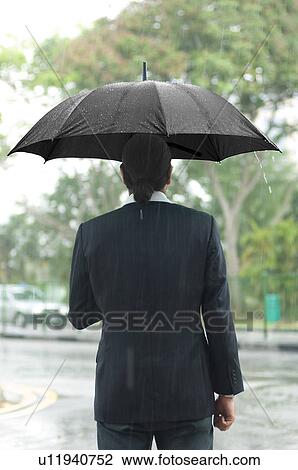 Rear view of a mid adult man holding an umbrella View Large Photo Image Stock Image - Rear view of a mid adult man holding an umbrella. Fotosearch