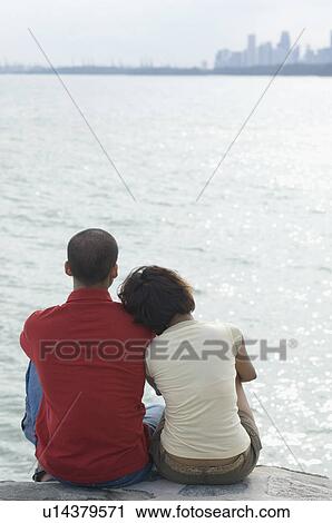 Stock Image - Rear view of a mid adult woman and a young man sitting on the beach. Fotosearch