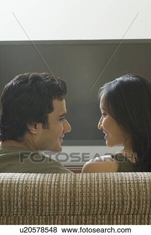 Rear view of a young couple sitting on a couch and looking at each other in front of a television View Large Photo Image Stock Photo - Rear view of a young couple sitting on a couch and looking at each other in front of a television. Fotosearch