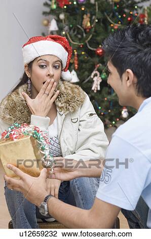 Stock Image - Rear view of a young man giving a Christmas present to a young woman. Fotosearch