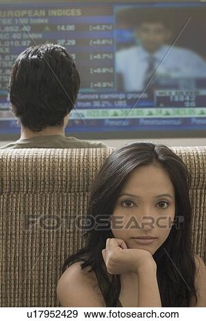 Stock Photo - Rear view of a young man watching television with a young woman sitting behind him. Fotosearch