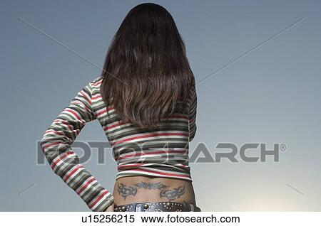 Stock Photography - Rear view of a young woman standing with a tattoo on her back. Fotosearch