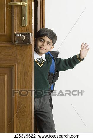 Stock Image - Schoolboy standing at a door and waving. Fotosearch