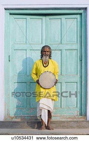 Stock Image - Senior man standing at the entrance of a house and holding a tambourine. Fotosearch