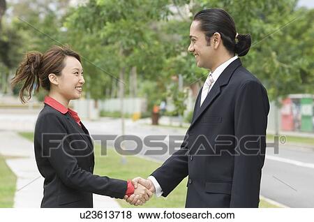 Side profile of a businessman and a businesswoman shaking hands and smiling View Large Photo Image Stock Photo - Side profile of a businessman and a businesswoman shaking hands and smiling. Fotosearch