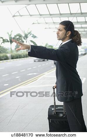Stock Image - Side profile of a businessman hailing a taxi. Fotosearch