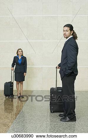 Side profile of a businessman holding his luggage with a businesswoman standing in the background View Large Photo Image Stock Image - Side profile of a businessman holding his luggage with a businesswoman standing in the background. Fotosearch
