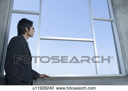 Stock Image - Side profile of a businessman looking through a window. Fotosearch