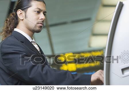 Stock Image - Side profile of a businessman using an automatic ticket machine. Fotosearch
